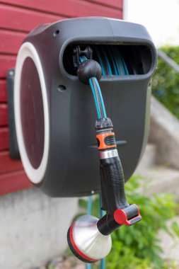 Duvar monte edilebilir hortum makarası. Ev duvarına fıskiye asılmış modern bahçe sulama hortumu. Çim ve bitki ağacı akıllı sulama su sistemi ekipmanı aracı.