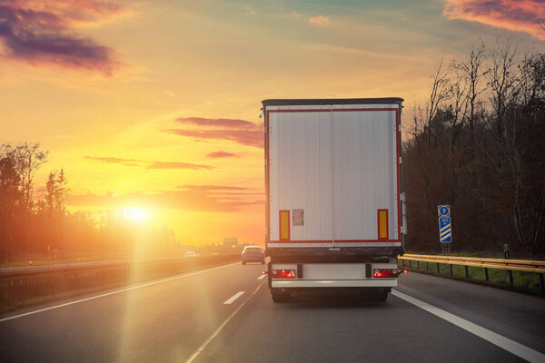 Tail view white blank modern delivery big shipment cargo commercial semi trailer truck moving motorway road city urban suburb. Business distribution logistics service. Lorry driving highway sunset.