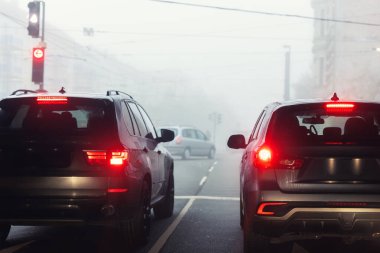 Manzaralı şehir trafiği trafik sıkışıklığı sisli, yağmurlu, sisli, sisli sabah, düşük görüş mesafesi soğuk bahar mevsiminde birçok arabayı cezbeder. Mevsimsel kötü yağmurlu hava kazası tehlike uyarısı araba sisi uyarısı.