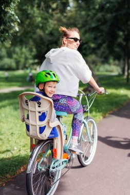 Gülümseyen mutlu aile, güneşli bir günde Avrupa sokaklarında bisiklet sürmekten hoşlanıyor. Parkta bisikletle gezen çocuklu bir anne. Güvenli bebek sandalyesinde oturan çocuk. Sağlıklı yaşam tarzı aktiviteleri.