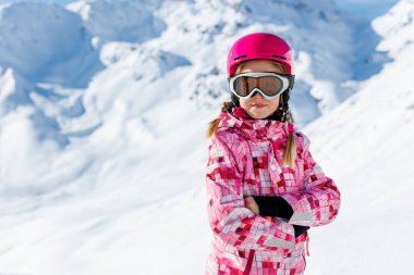 Kasklı, gözlüklü ve parlak takım elbiseli kayak yapan kendine güvenen sevimli beyaz çocuk portresi kışın ekstrem spor aktivitelerinin keyfini çıkarın. Dağlarda kayak yapan küçük bir çocuk..