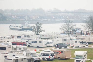 Warnemunde Rostock limanı kanalı yolcu gemisi iskelesi feribot arkaplanındaki karavan karavanı otoparkında. Birçok eğlence aracı Almanya limanı sisli gününde park etti. Seyahat macerası.