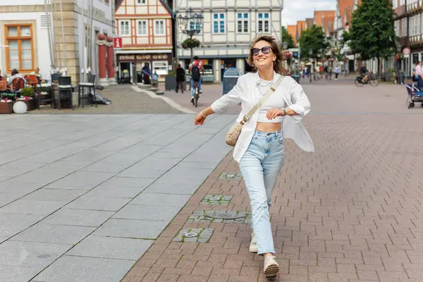 stock image Happy smiling young adult woman arms raised in excitement enjoys walking sunny day in historic town Celle city square. Female person smiling portrait. Freedom carefree people  concept.