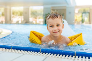 Küçük sevimli beyaz, sevimli sarışın çocuk havuz kenarında havuz kenarında otururken şişme kol bandı takıyor otel spa termal tatil köyüne gitmeden önce. Mutlu çocuk yaz tatili ailesinin tadını çıkar..