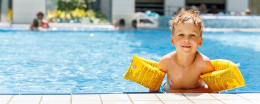 Küçük sevimli beyaz, sevimli sarışın çocuk havuz kenarında havuz kenarında otururken şişme kol bandı takıyor otel spa termal tatil köyüne gitmeden önce. Mutlu çocuk yaz tatili ailesinin tadını çıkar..