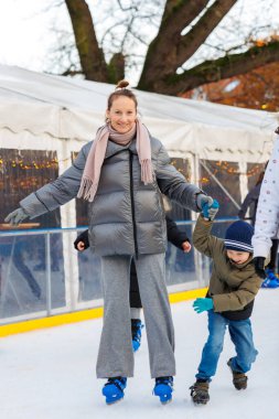 Genç, çekici, beyaz bir kadın kışın Avrupa 'nın eski şehirlerinde gezerken küçük oğluyla buz pateni pistinde eğleniyor. Anne ve çocuk tatil sporu aktiviteleri