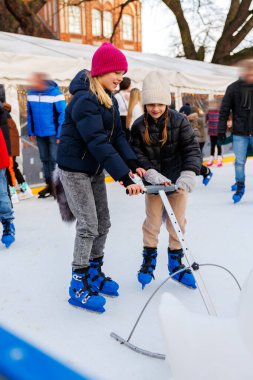 Young adult attractive beautiful caucasian woman enjoy having fun with little toddler son at outdoor skating rink while travel in old european city in winter. Mom and child holiday sport acitivities. clipart