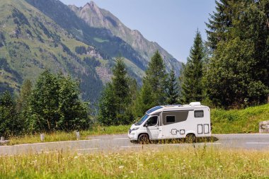 Manzaralı büyük beyaz aile karavan aracı Avrupa otoyolu Alp Dağları 'nı güneşli yaz gününde geçiyor. Karavanın yaşam tarzı macera turizmi Alpler seyahat konsepti.