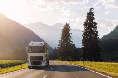 Manzaralı ön manzara modern beyaz yarı karavan kamyonu çarpıcı alp dağı yolu sıcak gün batımı aydınlık gökyüzü arka planı sürüyor. Kargo kargo lojistik taşıma aracı otoyolu akşam güneşi yolu.