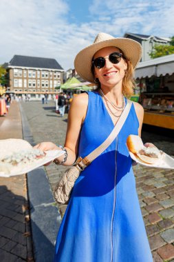 Portre genç, mutlu, yetişkin kadın turist Groningen Hollanda 'daki yerel markette geleneksel Hollanda sandviçi ve turşu turşusu ile soğan yemekten hoşlanıyor. Hollanda turizm beldesi.