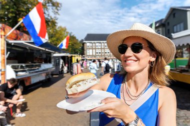 Portre genç, mutlu, yetişkin kadın turist Groningen Hollanda 'daki yerel markette geleneksel Hollanda sandviçi ve turşu turşusu ile soğan yemekten hoşlanıyor. Hollanda turizm beldesi.
