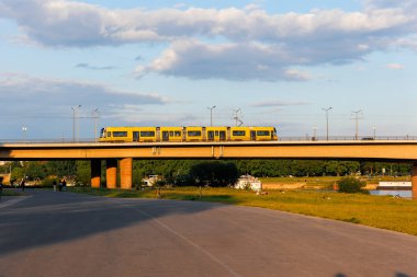 Yellow tram passes over the Carola Bridge in Dresden during sunset, casting warm light on the bridge and nearby riverbank, creating a scenic urban landscape. clipart