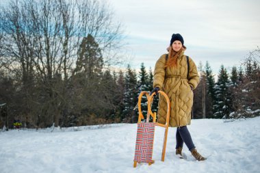 Portre genç, mutlu kadın, soğuk kış güneşli bir kış gününde eski ahşap retro-sledge dağ tepesine binerek eğleniyor. Neşeli kadın Noel sezonunda tepetaklak kayıyor..