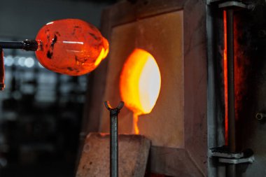 Endüstriyel zanaat atölyesindeki kırılma fırınının içinde erimiş cam şekilli cam boru aleti ile yakın plan cam üfleme. Avrupa 'nın el yapımı üfleme cam tasarımı üretimi.