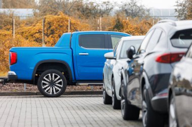 Açık otoparkın önüne park edilmiş mavi yeni bir kamyonet ya da sonbahar yeşilliklerine karşı park yeri. Modern SUV elektrikli araç dışarıda..