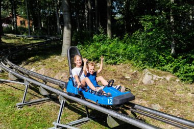 Bir çift sevimli gülen çocuk güneşli yaz günlerinde Harz doğa parkında birlikte alp hız trenine binerken eğleniyor. Çocuklar yaz tatillerinde aktif spor maceralarına çıkar..