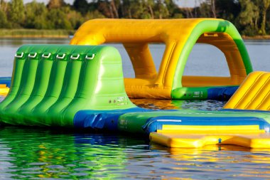 Şişme çocuklar güneşli bir günde göl havuzu yüzeyinde su parkı yüzüyor. Su parkı engelleri kursu trambolin trambolini açık deniz macerası oyun parkı çocukların tatil tatili.