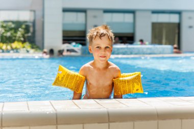 Küçük sevimli beyaz, sevimli sarışın çocuk havuz kenarında havuz kenarında otururken şişme kol bandı takıyor otel spa termal tatil köyüne gitmeden önce. Mutlu çocuk yaz tatili ailesinin tadını çıkar..