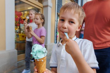 Portre sevimli neşeli çocuk sıcak yaz gününde ailesiyle birlikte Avrupa sokak yolunda dondurma yürüyüşü yapıyor. Komik çocuklar dışarıda tatlı vanilyalı dondurma yiyor..