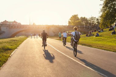 Manzaralı gençlik manzarası. Güneşli Dresden Elbe nehir kenarındaki yolda bisiklete binen insanlar günbatımının ışıltılı ve boş zamanlarına karşı. Atlılar tarihi Augustus Köprüsü 'nün yanında tekerlek gösterisi yapıyor. Kalabalık çim çayırını rahatlatıyor..