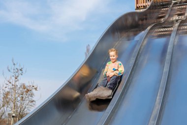 Sevimli, sevimli sarışın çocuk, güneşli bir günde parkın dinlenme yerinde oyun parkında hızlı sürmekten hoşlanıyor. Çocukların dışında yaz etkinliği.