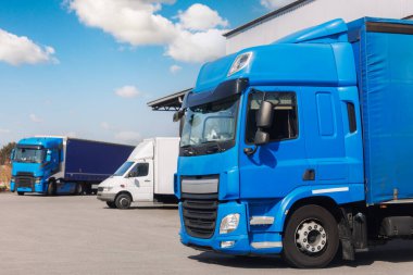 Modern mavi kargo kamyonu, lojistik deposu merkez kompleksinin dış bölümüne park etmiş. Yarı karavan kamyonu malları mavi gökyüzüne dağıtıyor. Kargo depolama tesisi endüstrisi