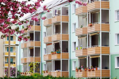 Alman eski ve yenilenmiş apartman binası cephesi ahşap balkonlar ve saksıda çiçekler. Kiraz pembesi çiçekleri bahar mevsimi yerleşim alanı. Emlak piyasası ve sigortası.