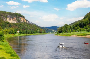 Panoramik manzaralı kiralık tekne Elbe Nehri eğrisinde Sachsische Schweiz Ulusal Parkı Almanya Koenigstein Whelen Dağları 'nda güneşli bir günde yol alıyor. Avrupa doğa gezisi hedefi.