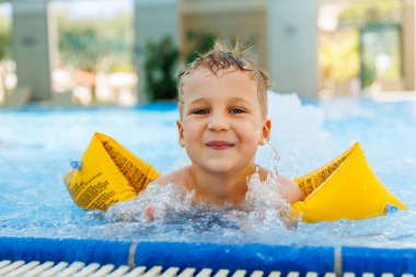 Küçük sevimli beyaz, sevimli sarışın çocuk havuz kenarında havuz kenarında otururken şişme kol bandı takıyor otel spa termal tatil köyüne gitmeden önce. Mutlu çocuk yaz tatili ailesinin tadını çıkar..