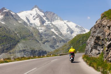 Motosikletli Grossglockner High Alpine Road Mountain Green Hills 'i kullanıyor. Dağlık arazide dolambaçlı bir yol manzaralı ve dağ turu deneyimi sunar..