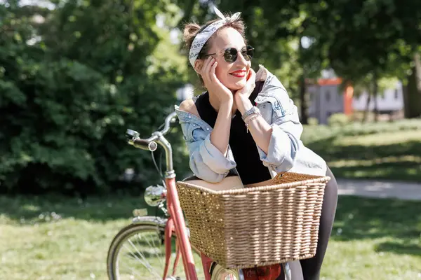 Portre genç, yetişkin, güzel bir kadın. Kırmızı antika bisikleti ve yeşil şehir parkı parlak güneşli yaz günü giysisi. Dışarıda bisiklete binen mutlu, güzel bir kadın. Sağlıklı yaşam tarzı.