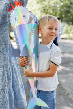 Gülümseyen çocuk Almanya 'daki ilk okulunda hediye dolu renkli köpekbalığı şekilli Schultuete tutuyor. Yüzgeçleri ve gözleri olan parlak koni yeni başlangıçlar için geleneği ve heyecanı simgeler..