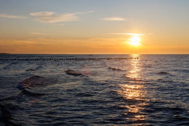 Baltık Denizi üzerinde gün batımının manzarası dalgalı dalgaların arasından yansıyarak parlak bir ışık yolu oluşturur. Tahta dalgalar ufka uzanıyor sakin bir deniz manzarası için sakin ritim..
