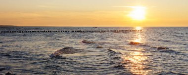 Baltık Denizi üzerinde gün batımının manzarası dalgalı dalgaların arasından yansıyarak parlak bir ışık yolu oluşturur. Tahta dalgalar ufka uzanıyor sakin bir deniz manzarası için sakin ritim..