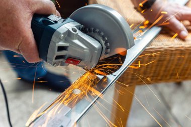 Bir kişi, bir açı öğütücüsüyle metali kesiyor ve farklı yönlere doğru parlak turuncu kıvılcımlar saçıyor. Yakın çekim çalışmanın gücünü, hassasiyetini ve yoğunluğunu yakalıyor..