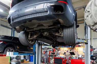 Sahne altı POV parçalanmış cip arabası kaldırılmış şanzıman kutusu atölye servis bakım istasyonunda asansörle kaldırılmış. Araç kontrolü ve onarımı. Alt gövde şasisi ve süspansiyon parçaları.