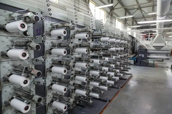 Fabrika ekipmanları perspektifte. Kumaş dokumak için polipropilen ipliklerle dolu sıralar. Otomatik makine. Kimse..