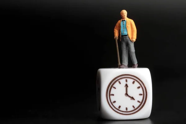 時計のシンボルの上に立つ老人のミニチュアフィギュア — ストック写真
