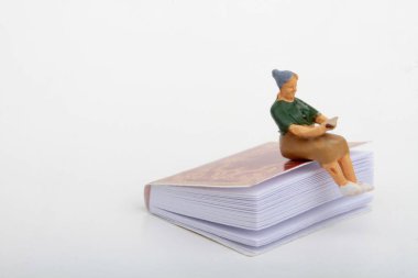 Yaşlı bir kadının minyatür biblosu dev bir kitabın üzerinde oturup kitap okuyor.