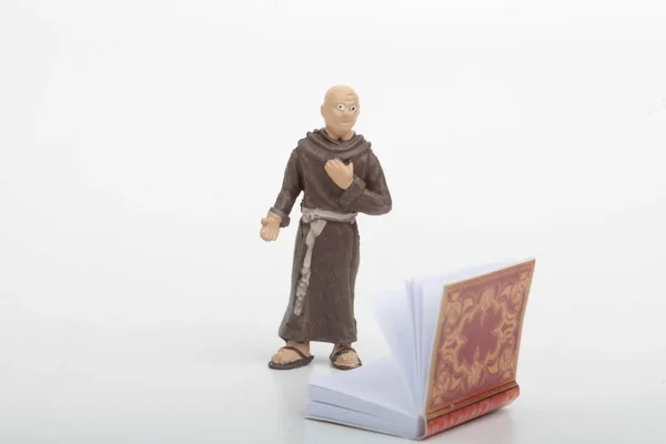 白い背景に古代の大きな本を持つ僧侶のミニチュアフィギュア — ストック写真