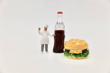 Şefin minyatür figürü yanında bir şişe kola tutuyor bir çizburger.