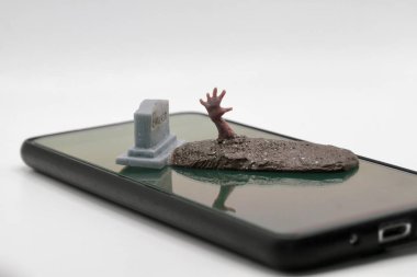 Akıllı telefonun ekranına yerleştirilmiş bir mezardan çıkan bir zombinin minyatür figürü.