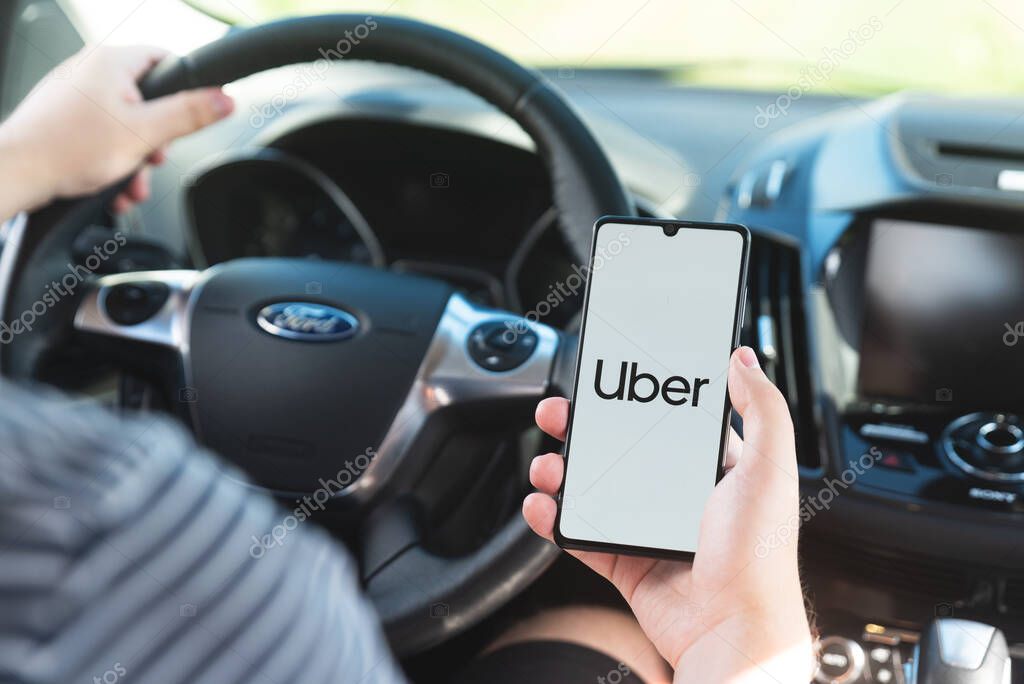 Wroclaw, Poland - AUG 25, 2020: Uber driver holding smartphone in car. Uber is sharing-economy service for ubran transport.