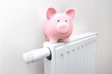 Evdeki radyatör, yükselen ısıtma fiyatları kavramı. Eşarplı domuz kumbarası radyatörün üstünde duruyor.