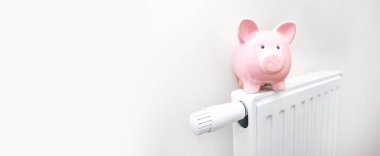 Evdeki radyatör, yükselen ısıtma fiyatları kavramı. Eşarplı domuz kumbarası radyatörün üstünde duruyor.