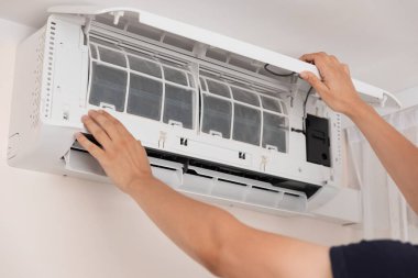 Elektrikçi içeride klima tamir ediyor. Adam havalandırma sistemini temizliyor.