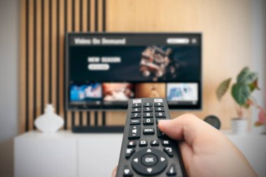 VOD servis ekranı. Adam elle uzaktan kumanda ile TV izlerken.