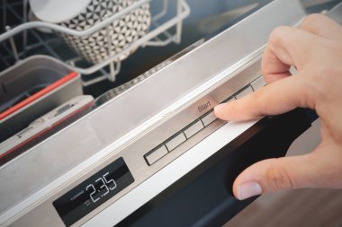 Bulaşık makinesinin kontrol panelinde başlat düğmesine basan adam.