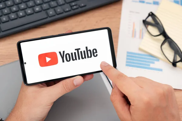 ポーランドのヴロツワフ Aug 2023 画面にYoutubeのロゴが付いているデバイスを保持する男 YoutubeはGoogleによって開発された最も人気のあるビデオサービスです ロイヤリティフリーのストック写真