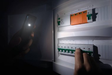 Blackout concept, energy crisis. Hand holding a flashlight to investigate a home fuse box
